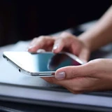 Close-up of two hands holding a smartphone over a dark surface