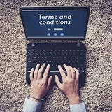 Hands typing on a laptop showing "Terms and conditions" on screen, viewed from above on carpet