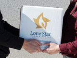 Two people handing off a white Lone Star Candle Supply shipping box outdoors