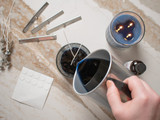 Overhead of hands pouring blue candle wax with wick pins, stickers, and a finished blue candle