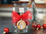 Glass jar with wooden lid wrapped in buffalo plaid ribbon and a red bow, tagged Merry Christmas with a silver deer