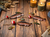 Three trout-shaped aroma-bead freshies with red-and-white bobbers and twine on weathered wood, lit candles and lures nearby