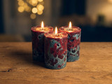 Three lit pillar candles with mottled red and gray pitted surfaces on a wood table, warm bokeh behind