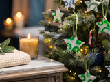 White star soap ornaments with green and blue swirls hanging on a lit Christmas tree beside a lit candle