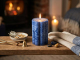 Lit blue fluted pillar candle on a wood beam with sage, brass wick trimmer and snuffer by a fireplace