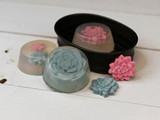 Teal and pink rose-shaped succulent soaps, some clear-cast, in and around a black oval tin