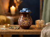 Blue wax melt cubes in the dish of a glowing brown ceramic warmer beside a lit candle