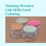 Four small glass jars with wooden lids stained tan, pink, green and mint, text reading Staining Wooden Lids With Food Coloring