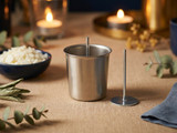 Metal votive mold with wick pin upright inside, a separate wick pin beside it, eucalyptus and tealights around