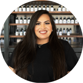 smiling woman with long dark hair in a black top before shelves of labeled black bottles
