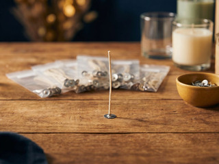 Single tabbed cotton wick standing upright on a wood table, bagged wick assortments and finished candles behind