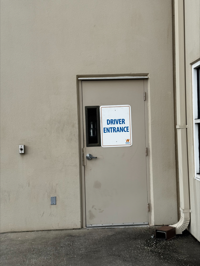 Gray metal door on a beige warehouse wall marked with a Driver Entrance sign