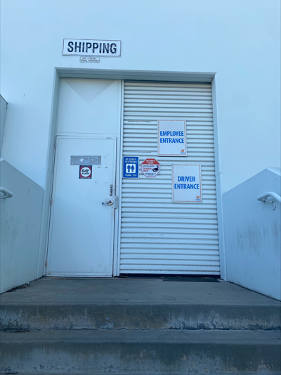 White warehouse roll-up door under a SHIPPING sign with Employee Entrance and Driver Entrance placards