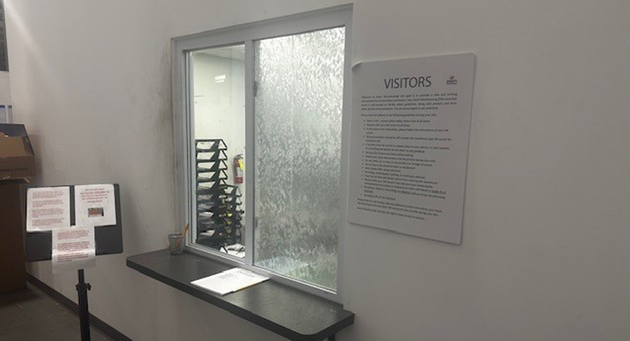 Indoor visitor pickup window with a posted visitor instructions notice beside it
