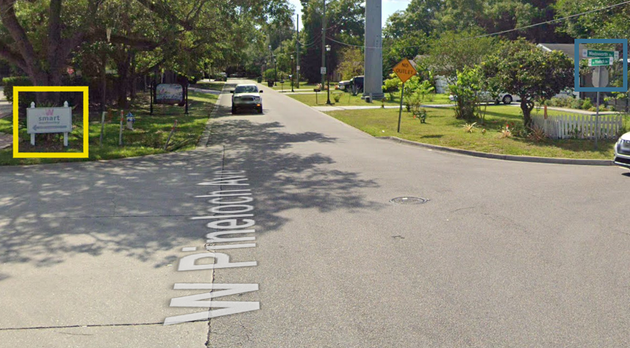 Tree-lined residential street with a yellow box marking the driveway turn-in on the left