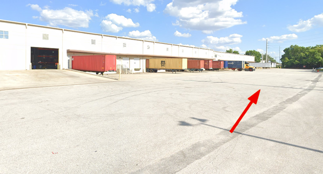 Warehouse truck court with dock doors and trailers, a red arrow pointing right toward the west side