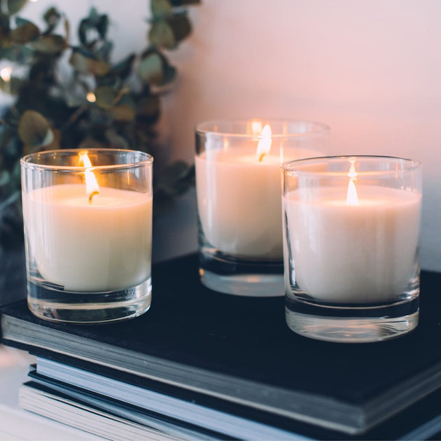 Three lit cream candles in clear glass tumblers on stacked black books beside eucalyptus