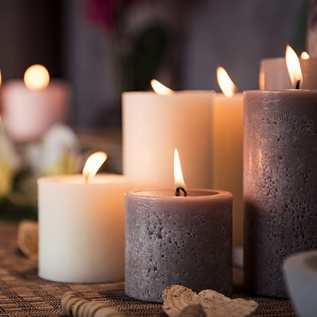 Cluster of lit cream and grey pillar candles of varying heights with seashells on a bamboo mat