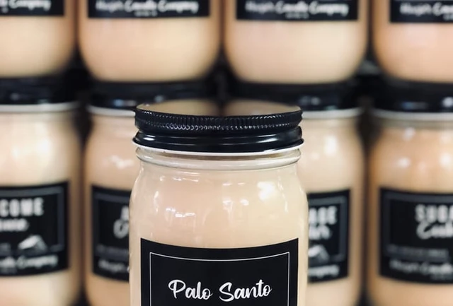 A Hoosier Candle Company Palo Santo mason-jar candle in front of rows of matching black-labeled jar candles