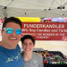 Two smiling makers at their market tent beside a red Funderkandles banner reading 90% Soy Candles and Tarts