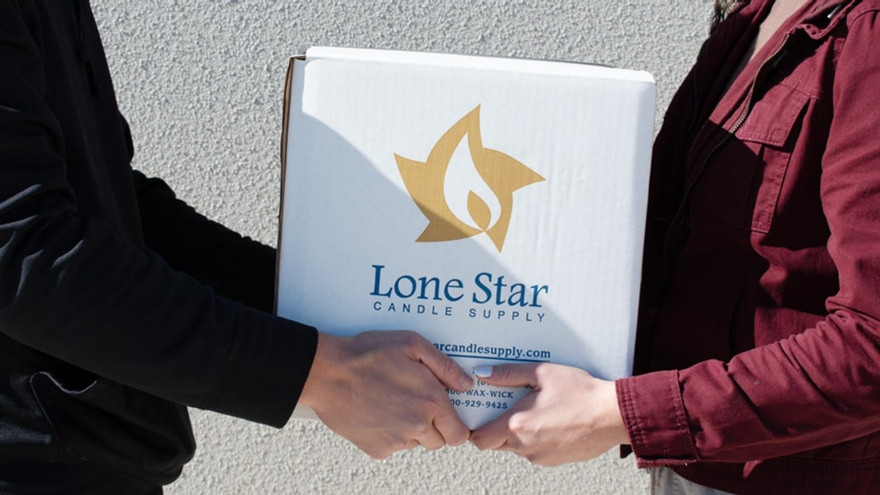 Two people handing off a white Lone Star Candle Supply shipping box outdoors