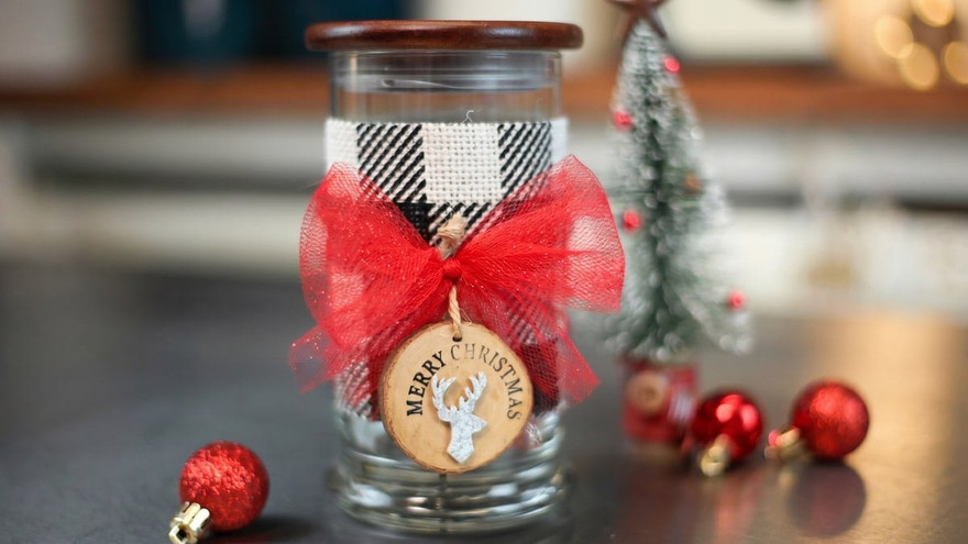Glass jar with wooden lid wrapped in buffalo plaid ribbon and a red bow, tagged Merry Christmas with a silver deer
