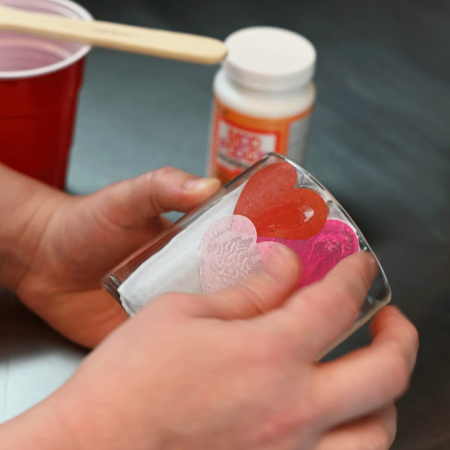 hands smoothing overlapping red and pink tissue paper hearts onto a glass jar