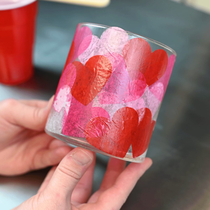 hand holding a glass jar covered in overlapping red and pink tissue paper hearts