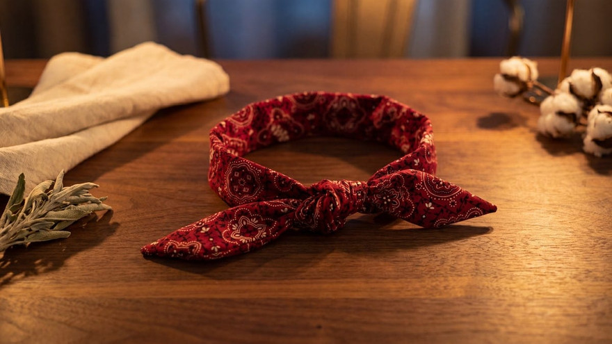 Red paisley bandana cooling neck wrap tied in a knot on a wood table, cotton stems and sage sprig nearby