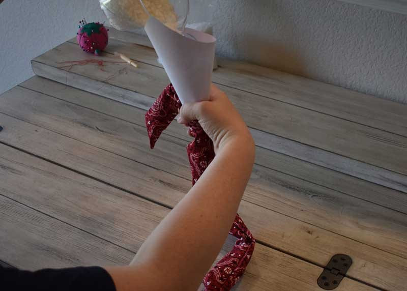 Hand pouring water crystals into the red bandana tube through a rolled white paper funnel