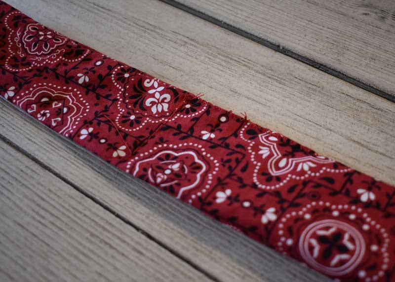 Close view of the finished stitched seam on the red paisley bandana fabric tube on gray wood