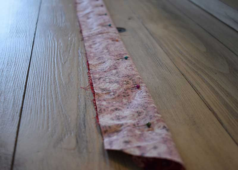 Long red fabric strip folded inside out and pinned along its open edge on a wood floor