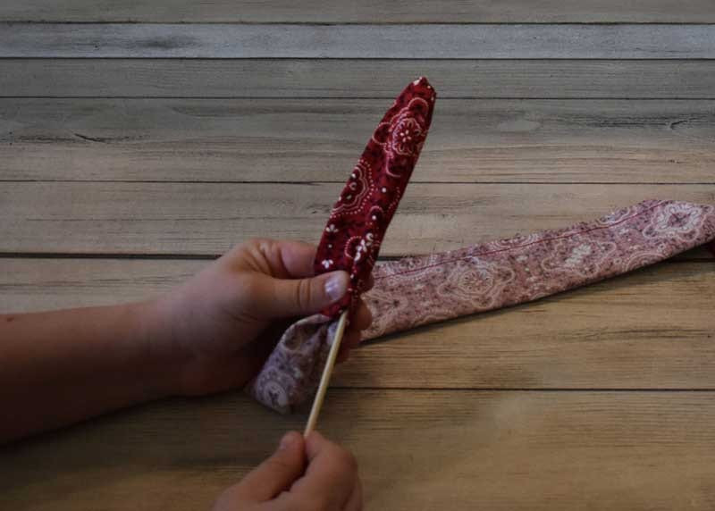 Hands turning the sewn bandana fabric tube right side out using a wooden dowel