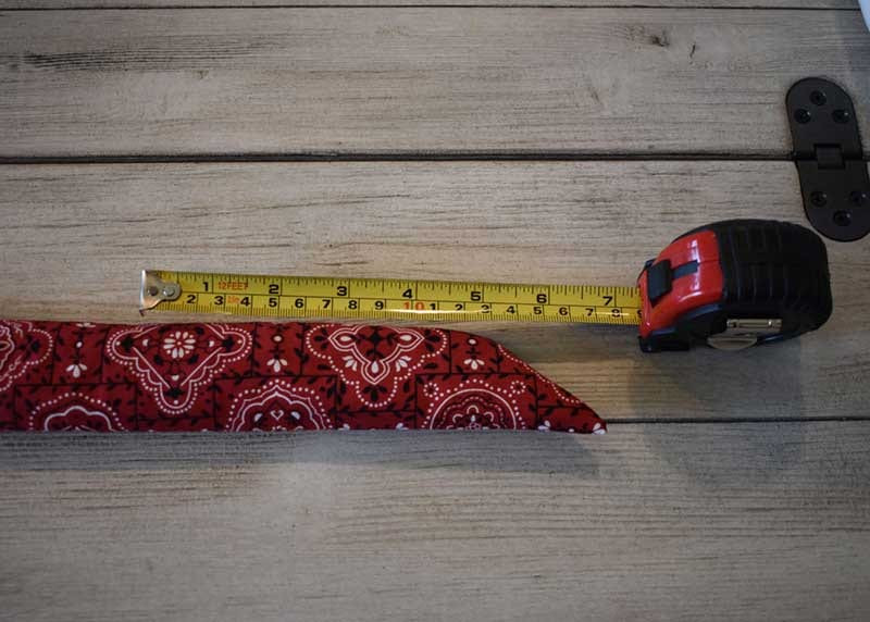 Yellow tape measure laid alongside the turned red bandana fabric tube on gray wood