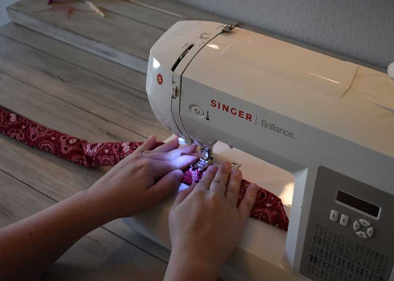 Hands stitching a seam across the red bandana fabric tube on a Singer Brilliance sewing machine