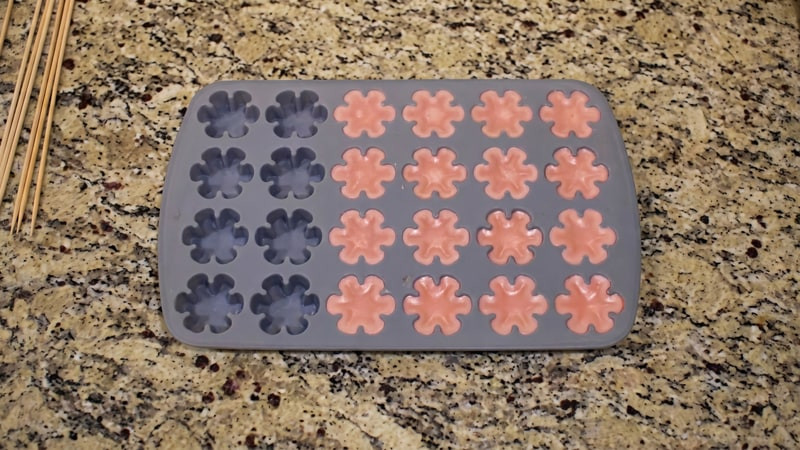 Gray flower silicone mold holding cooled navy-blue and pink wax tarts on a granite counter