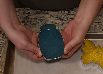 Hands holding a blue mason-jar-shaped beaded freshie with a small pin set in the top edge