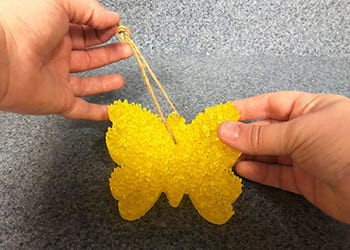 Hands threading a tan twine loop through the top of a yellow butterfly freshie