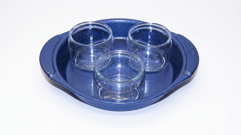Three clear glass candle jars arranged in a round blue metal baking pan