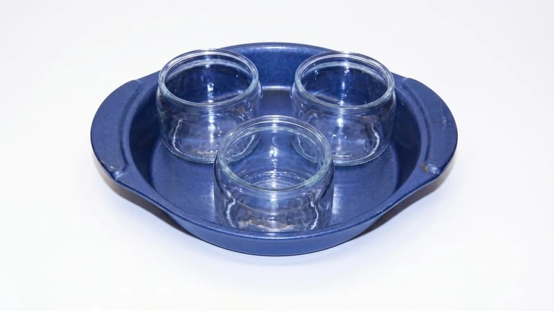 Three clear glass candle jars arranged in a round blue metal baking pan