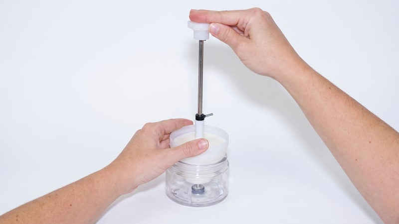 Hands pressing a wick into the bottom of a glass jar with a white wick-setting tool
