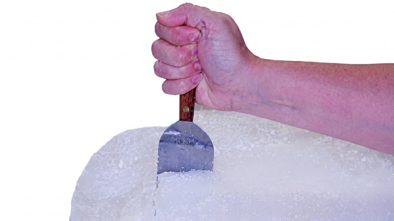 Hand pressing a wood-handled metal scraper into a block of white candle wax