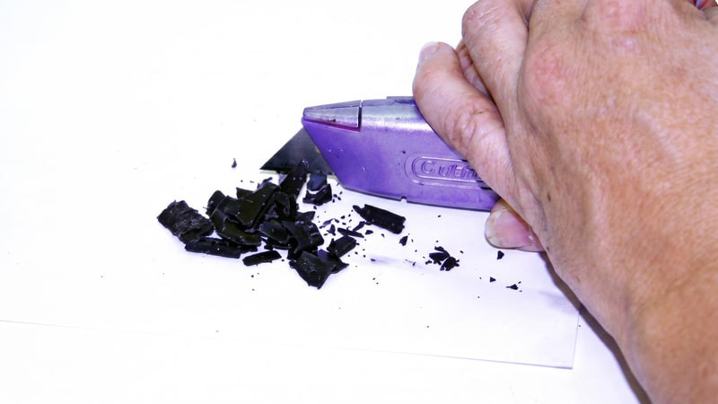 Hand shaving chips from a black dye block with a purple Cutter blade onto white paper