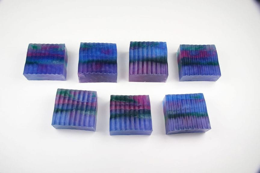 Seven ridged-bottom galaxy soap bars in blue, purple, magenta, and green lined in two rows