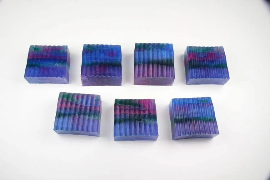Seven ridged-bottom galaxy soap bars in blue, purple, magenta, and green lined in two rows