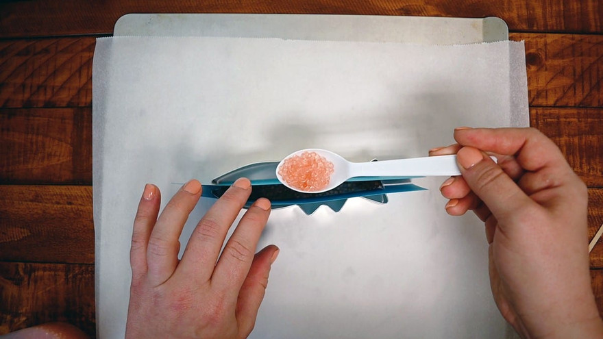 White measuring spoon of pink aroma beads poured into one side of a divided fish cutter on parchment