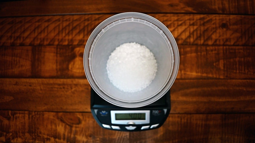 Overhead view of white aroma beads in a clear container on a digital scale reading 400, on a wood table
