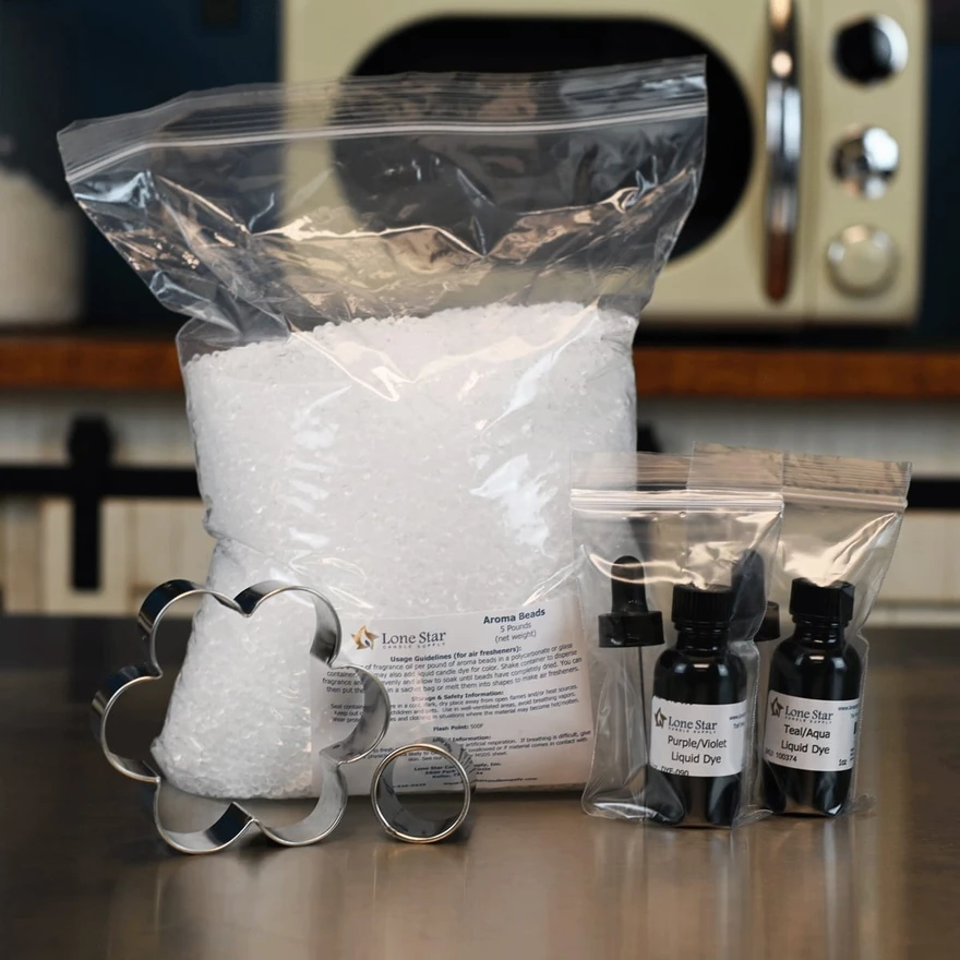 Bag of white aroma beads, flower cookie cutters, fragrance oil bottles, and liquid dye packets on a counter