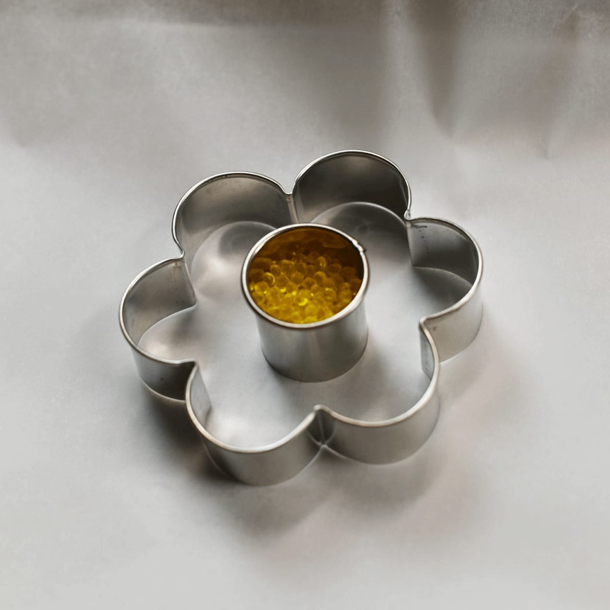 Round cutter filled with yellow aroma beads placed in the center of a flower cookie cutter