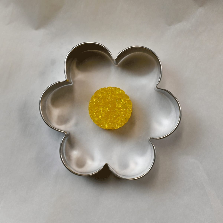 Baked yellow bead center sitting inside an empty flower cookie cutter on parchment paper
